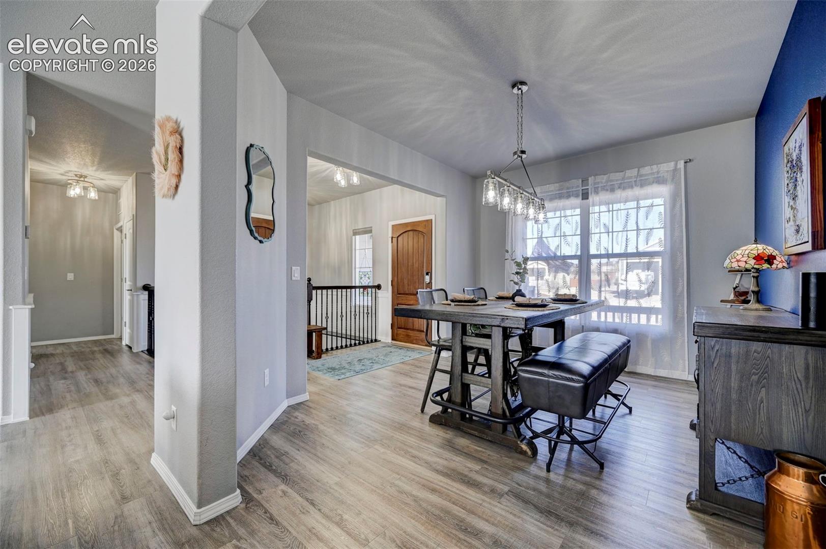 Open-concept dining area featuring wood-finish flooring, a contemporary linear chandelier, and a large window with sheers