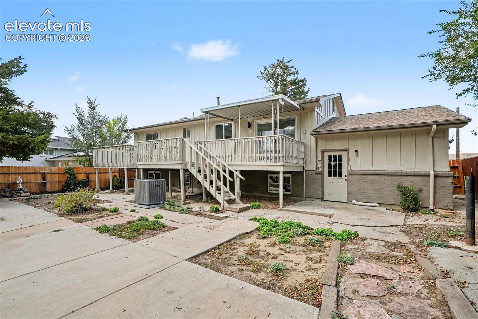 Exterior rear elevation featuring a covered wood deck, wood-railing staircase, concrete patio, and board-and-batten siding