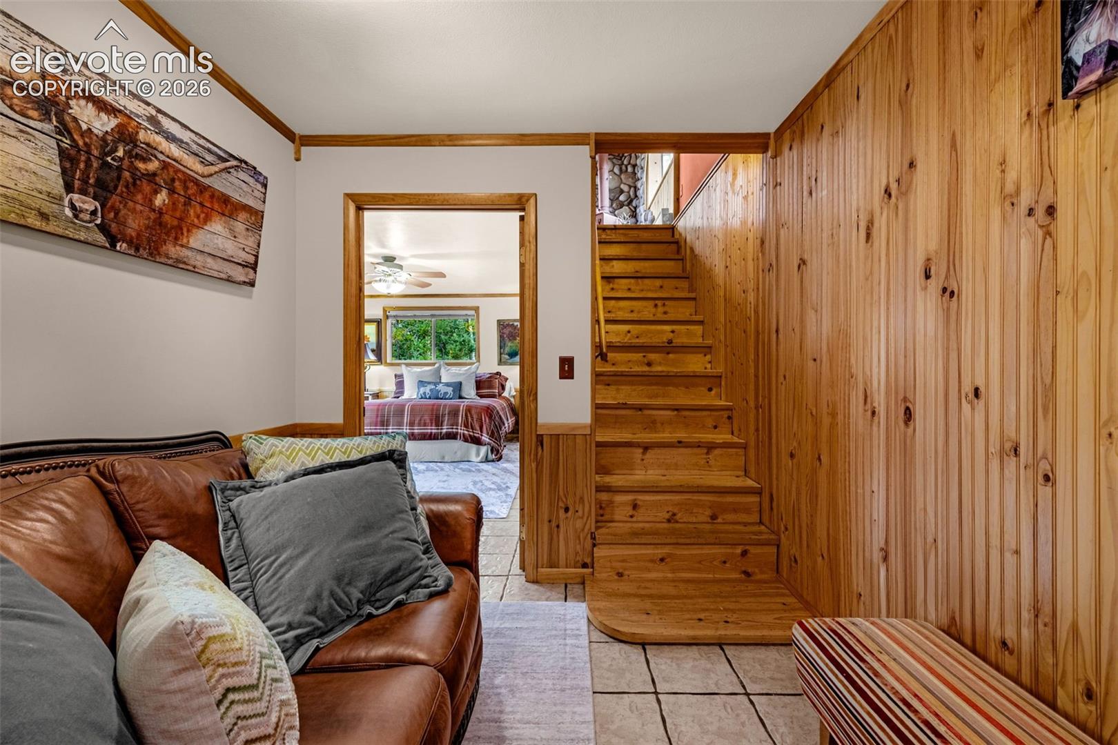 Interior space featuring vertical wood-plank wall paneling, natural wood staircase, tile flooring, and wood door casing