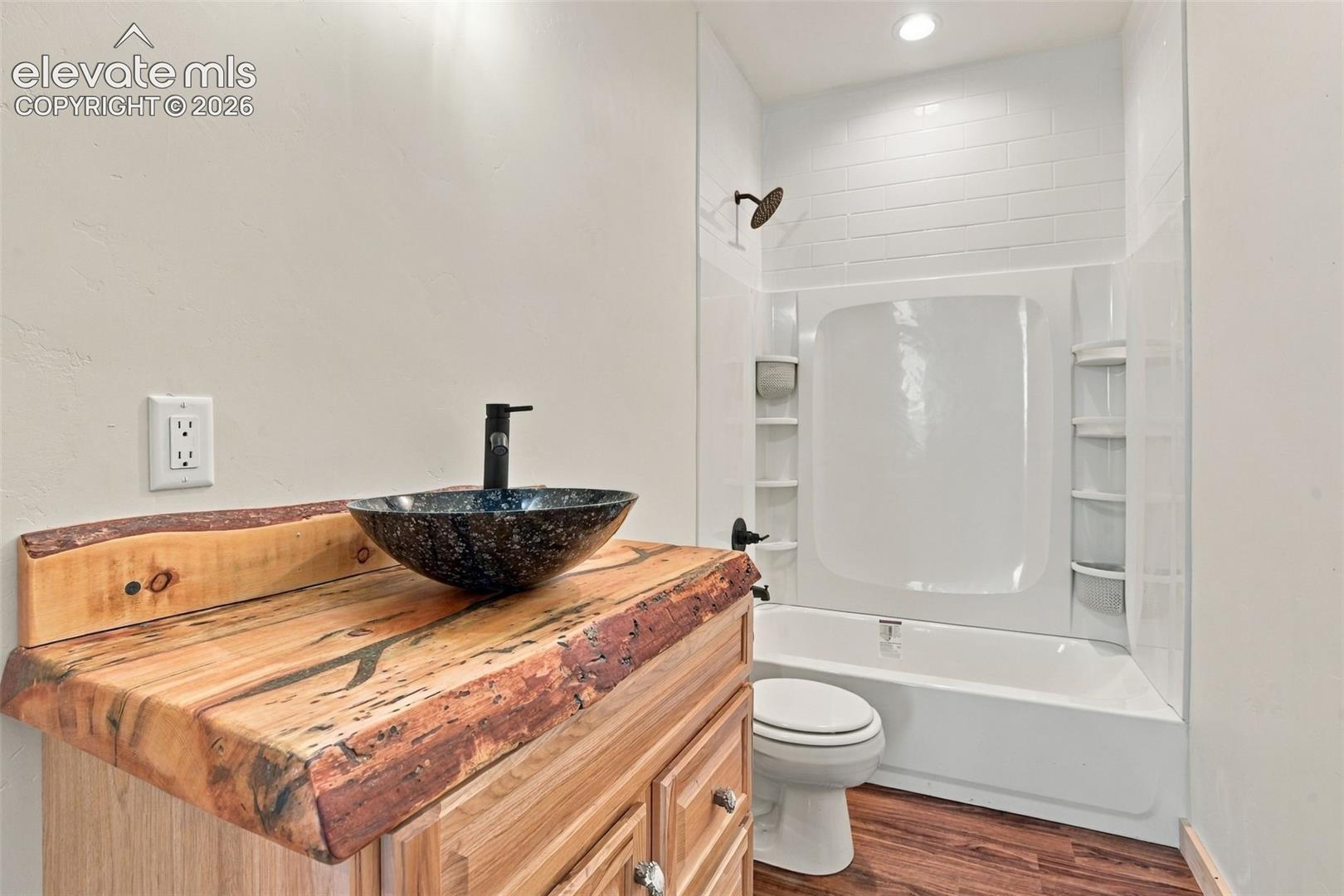 Bathroom featuring a live-edge wood vanity countertop, vessel sink, matte black hardware, wood-finish flooring, and a tub-shower combination with tile-surround detail