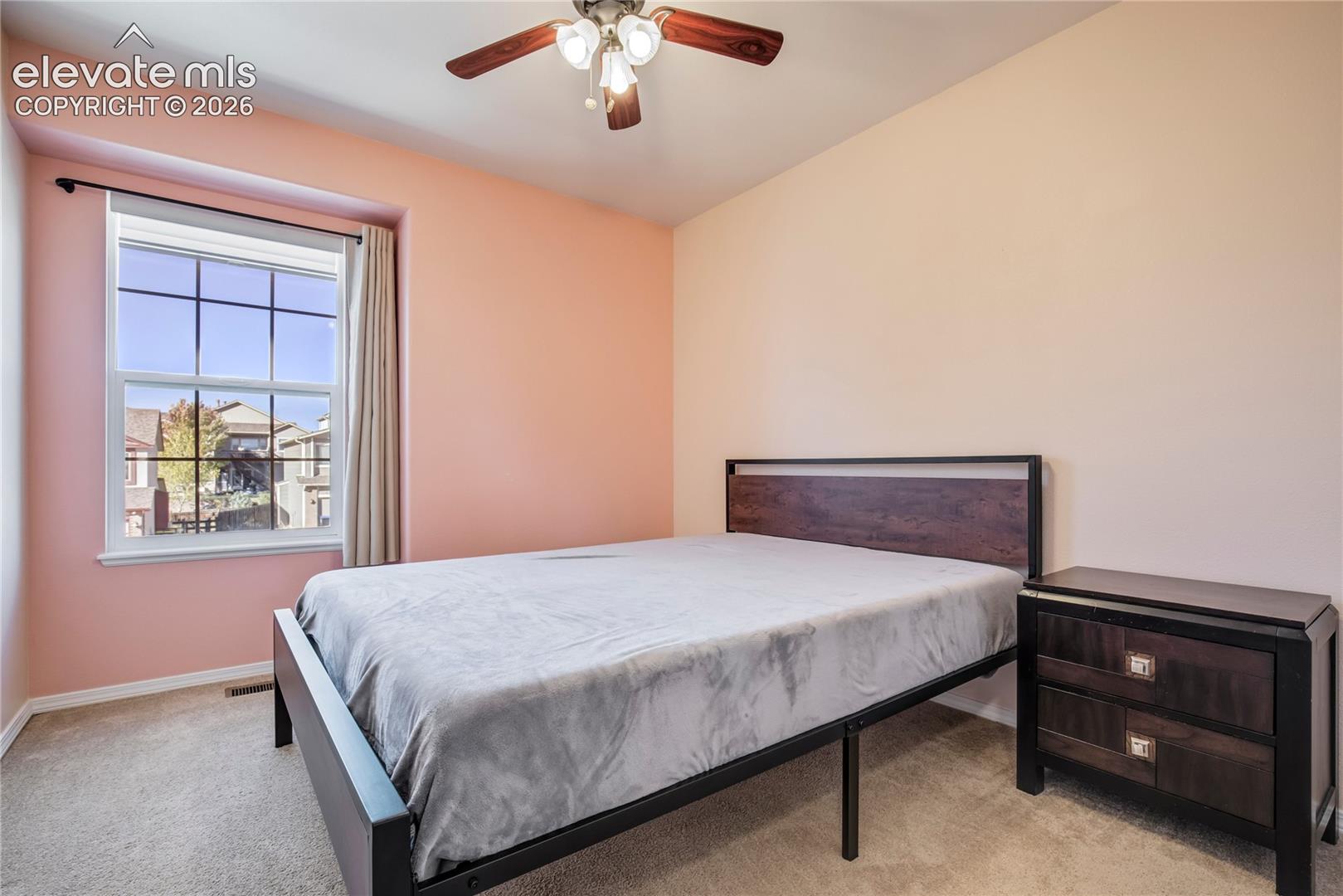 This comfortable upper-level bedroom features a ceiling fan, carpeting + a large window overlooking the neighborhood.