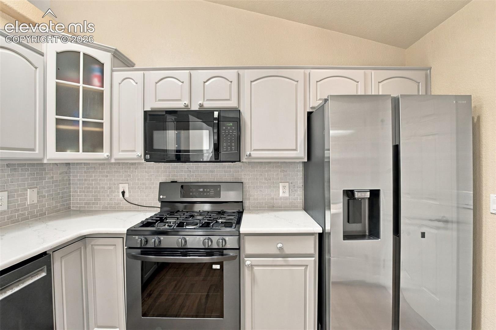 Kitchen featuring light-toned cabinetry, quartz countertops, subway tile backsplash, and stainless steel appliances including a gas range and built-in microwave