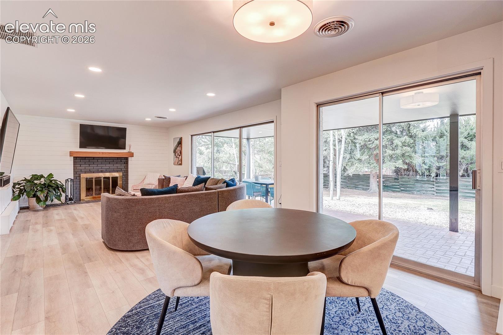 Open-concept interior featuring wood-finish flooring, a fireplace with a dark brick surround, shiplap accent wall, and recessed lighting