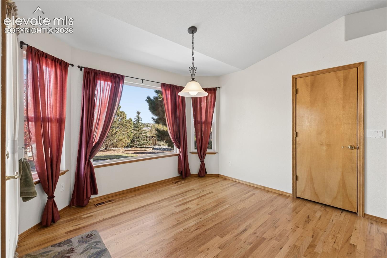 Wood-finish flooring, vaulted ceilings, bay window, and a hanging pendant light fixture
