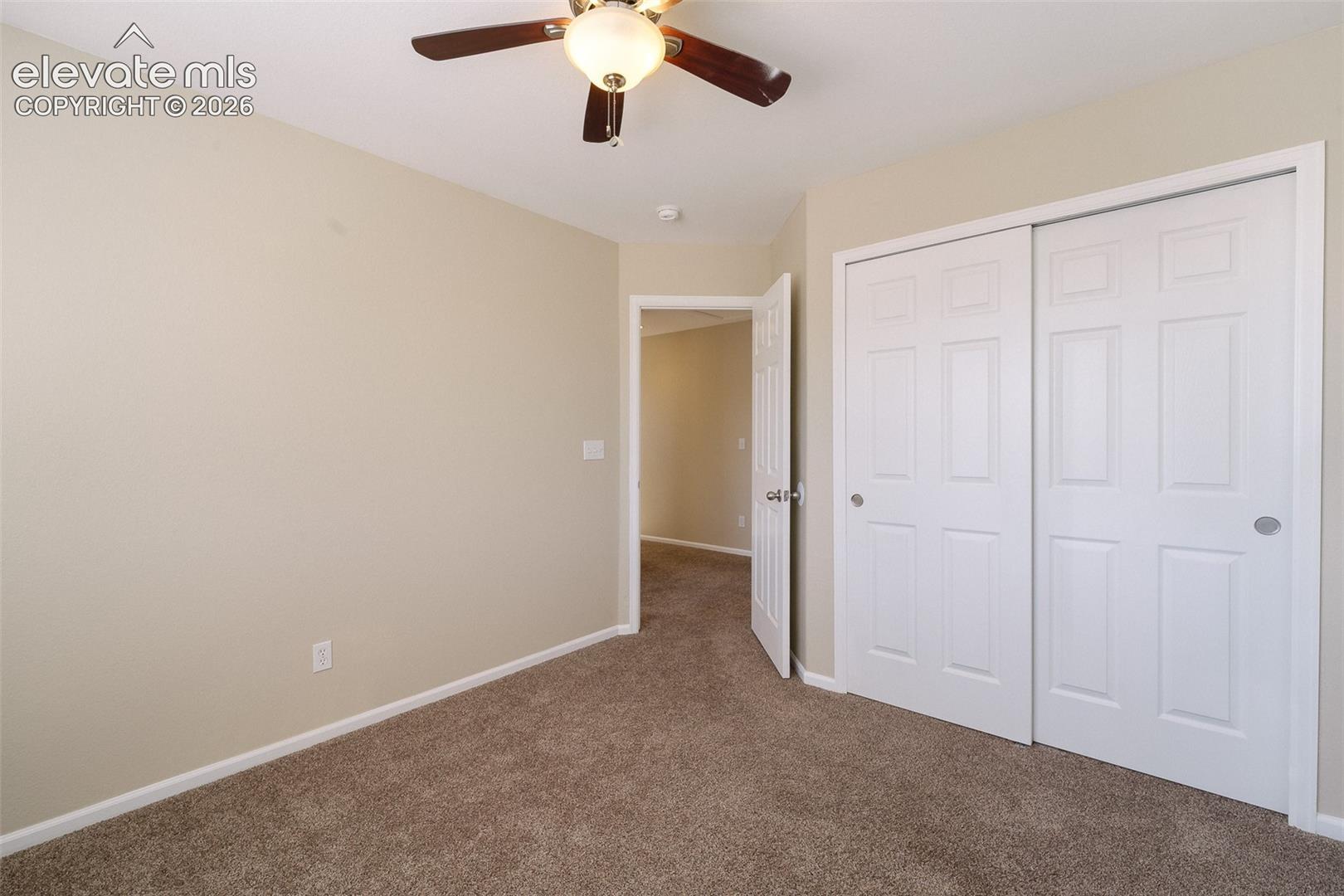 Neutral-toned interior room featuring wall-to-wall carpeting, a ceiling fan with integrated light fixture, and a white sliding-panel closet