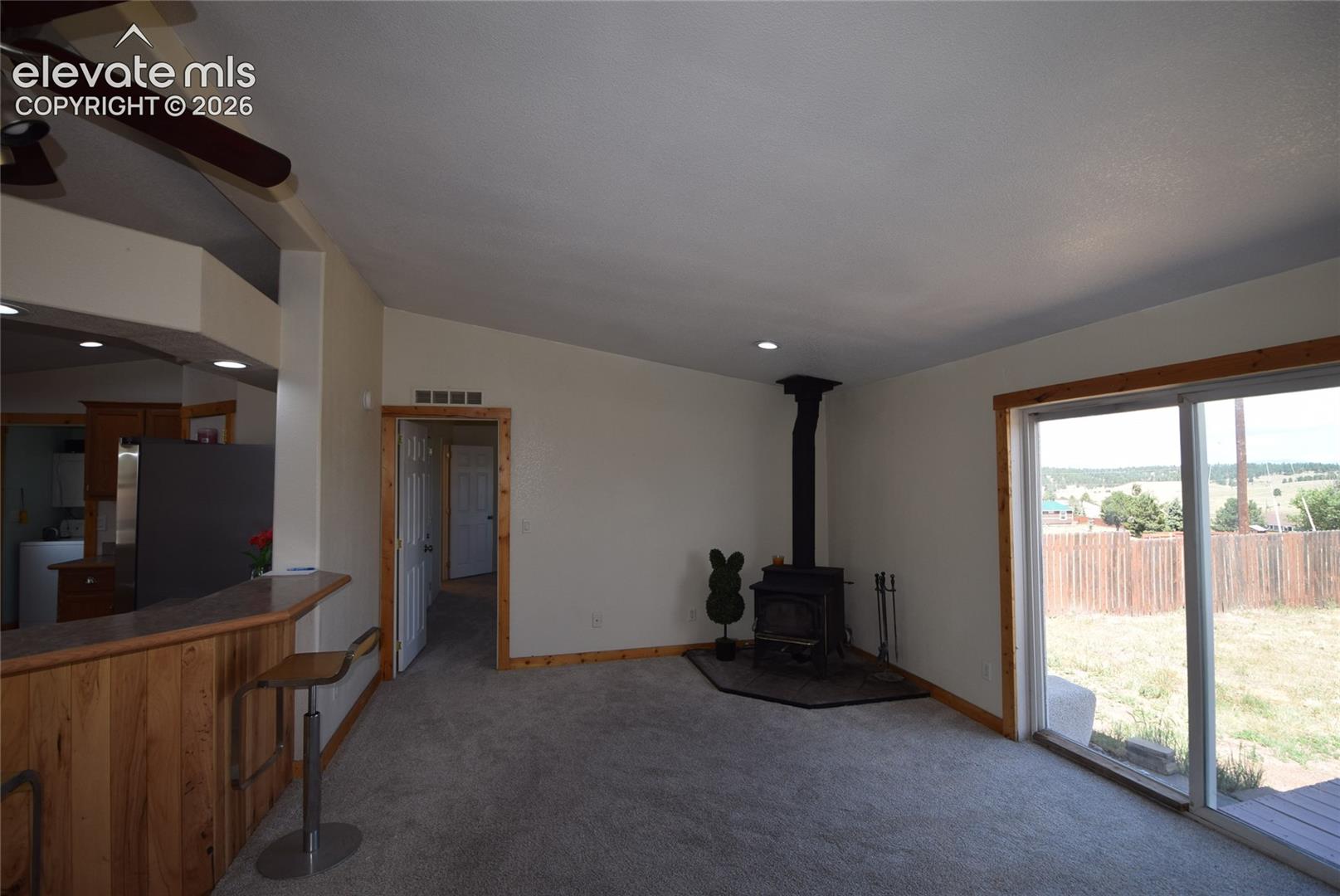 Sliding glass doors, wood-paneled breakfast bar, vaulted ceilings, recessed lighting, and a wood-burning stove