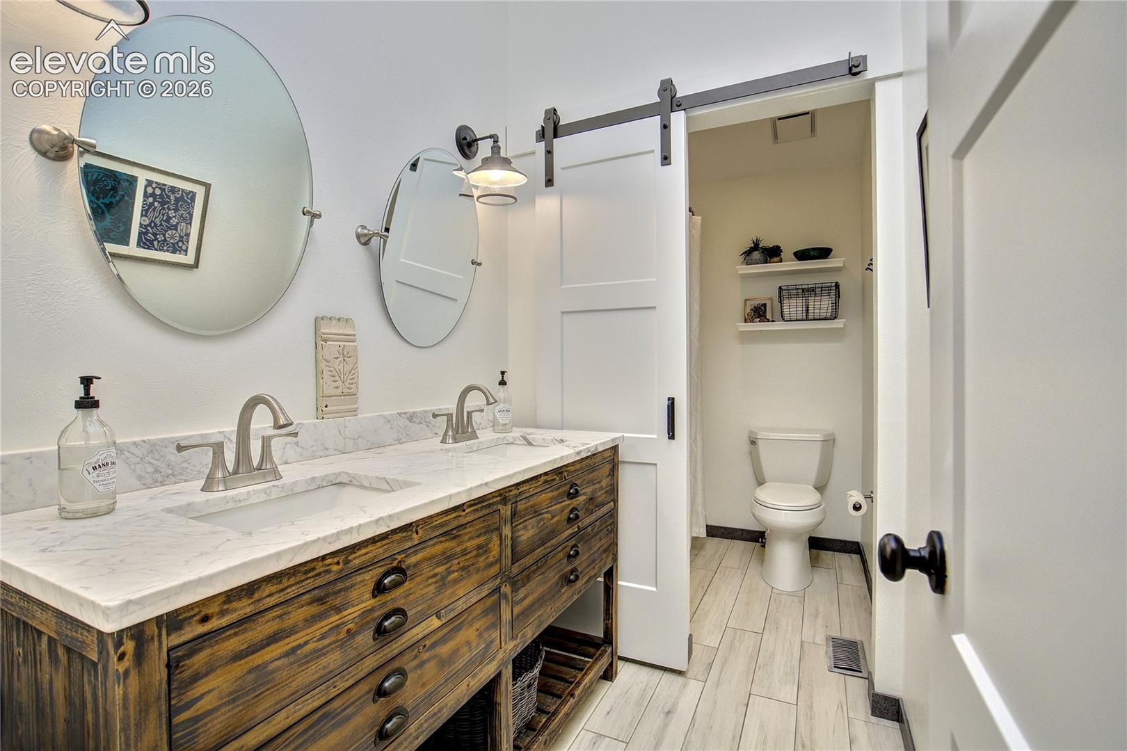 Completely remodeled with a dual-sink vanity,  wood-look tile + distinctive barn-door detail.