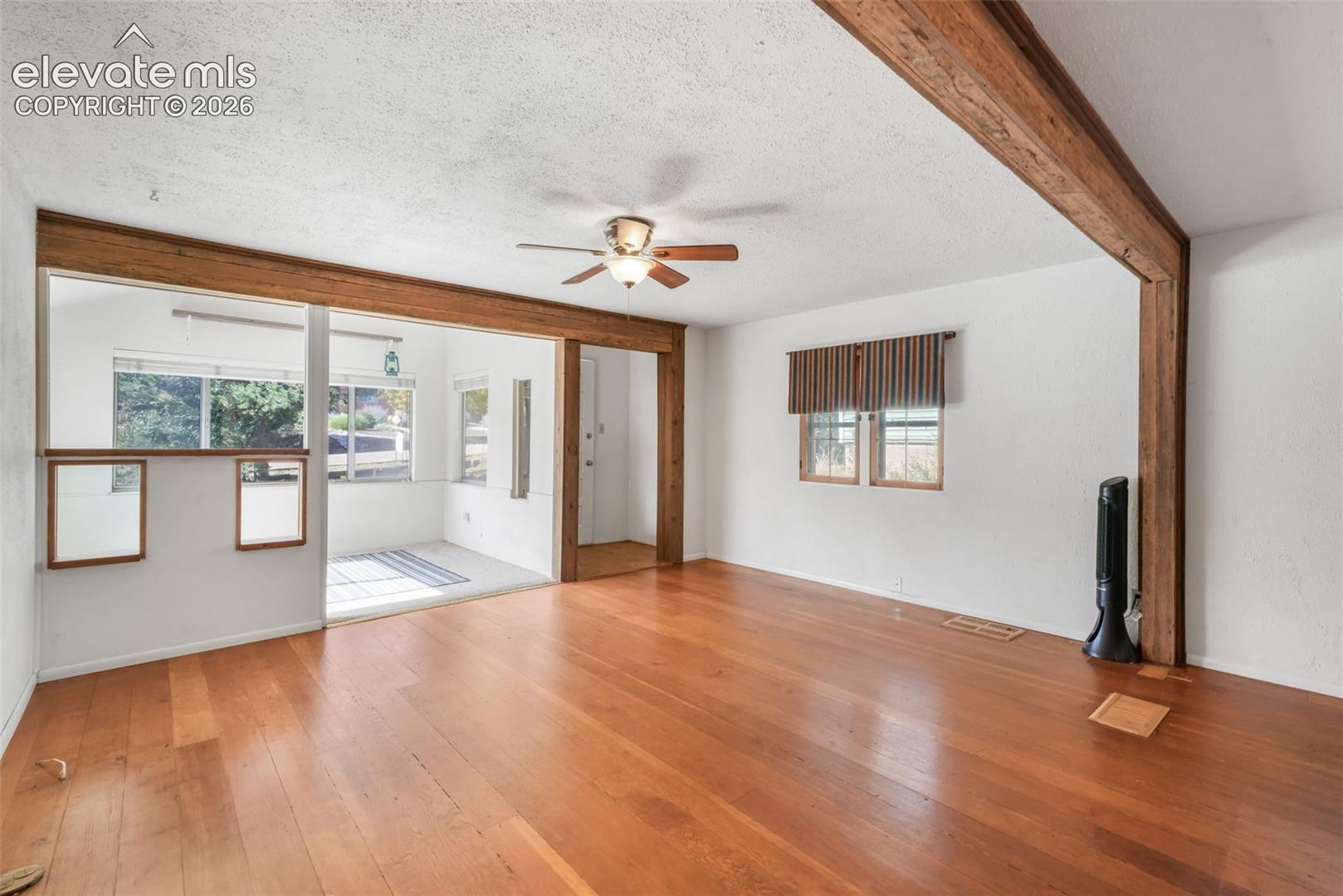 Hardwood flooring, exposed wood beams, ceiling fan, and multiple windows