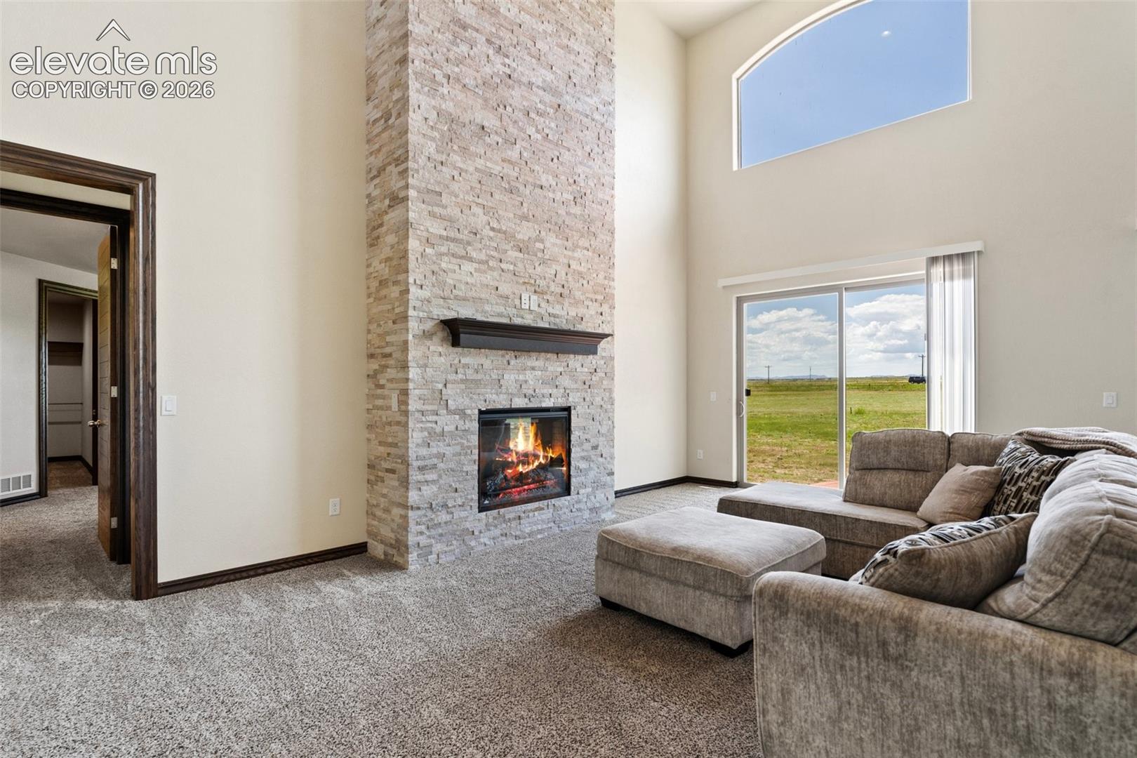 Vaulted living area featuring high arched windows, a stone fireplace, and sliding glass doors to the exterior