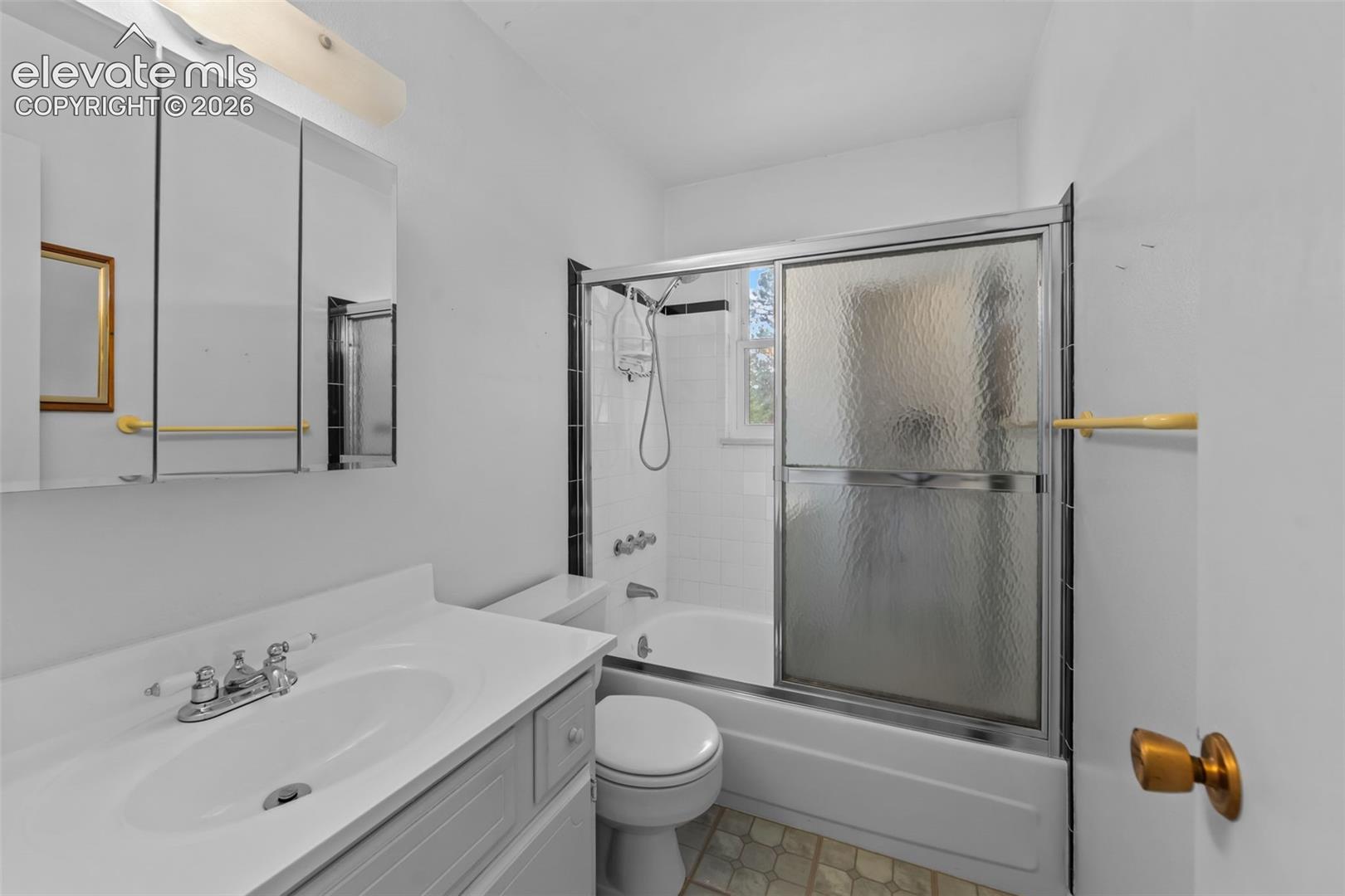 White vanity with integrated sink, three-door mirrored medicine cabinet, white bathtub with sliding textured glass doors, tiled shower surround, and a window providing natural light