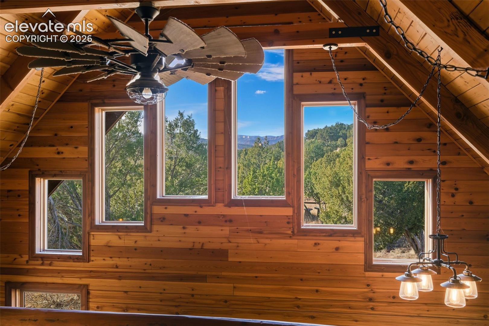 Vaulted wood-paneled ceiling with exposed beams, multiple windows, large ceiling fan, and chandelier lighting