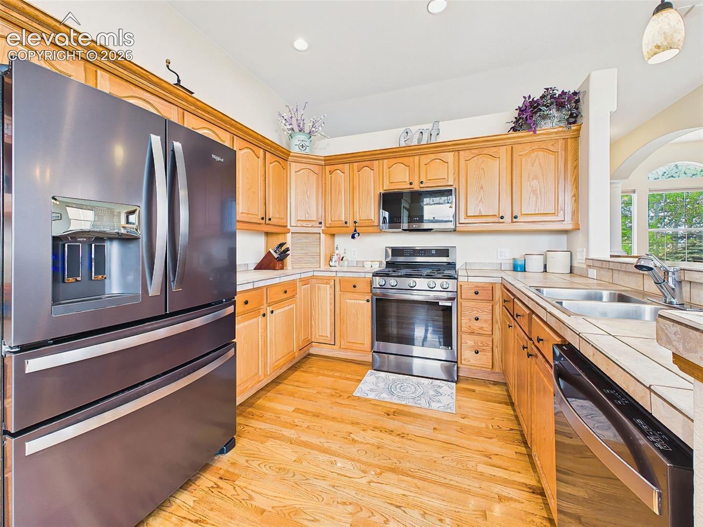 Well-appointed kitchen with tile countertops, recessed lighting, under-counter lighting, stainless steel appliances, and ample cabinet storage.