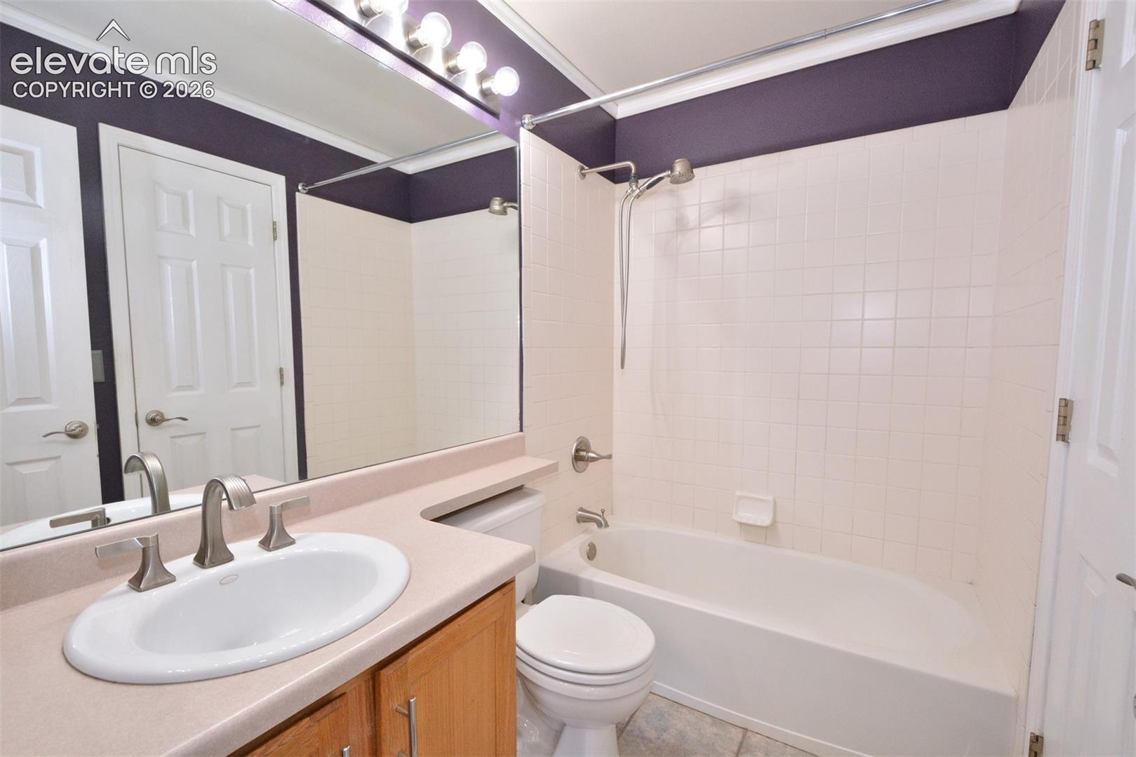 Spacious bathroom featuring a single vanity with wood cabinetry, a large vanity mirror, a built-in bathtub with shower, and tile flooring
