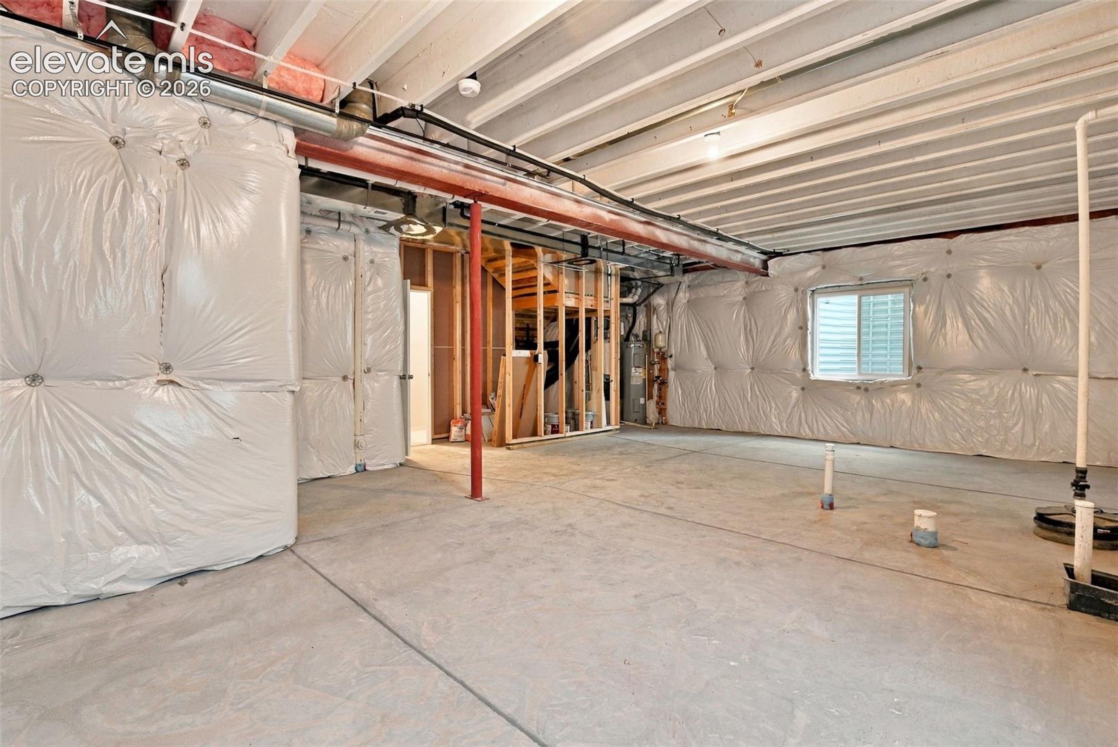 Unfinished basement space featuring exposed ceiling joists, concrete flooring, perimeter wall insulation, structural steel support columns, and an egress window