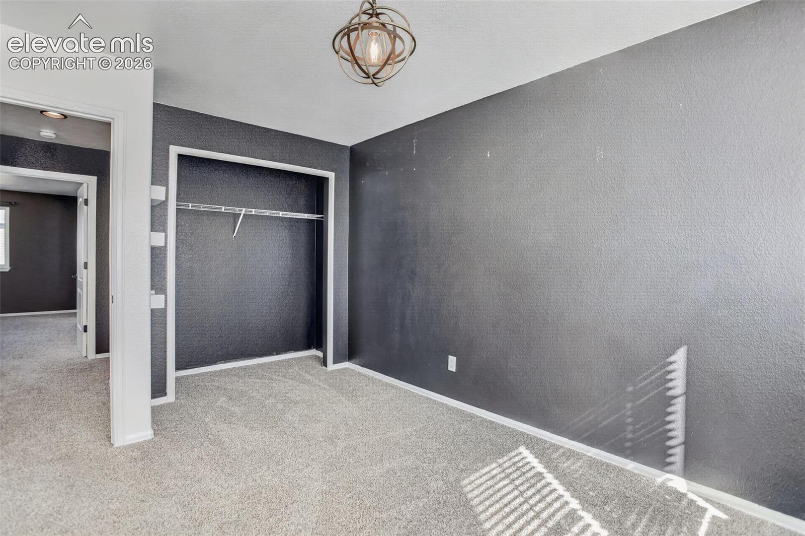 Carpet flooring, textured walls, built-in closet with shelving and hanging rod, overhead decorative light fixture