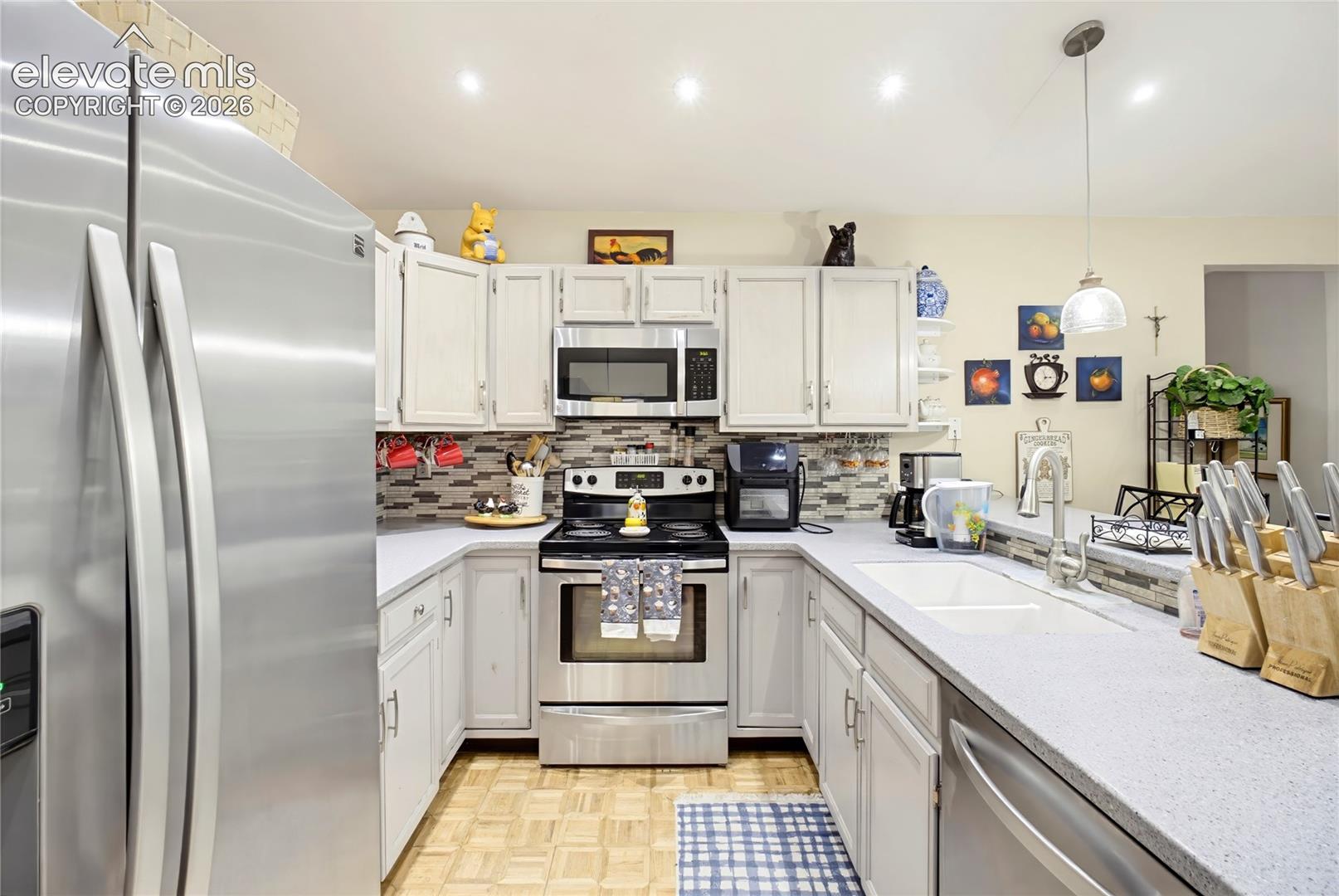 Stainless steel appliances, light-toned cabinetry, light-colored countertops, tile backsplash, and recessed lighting
