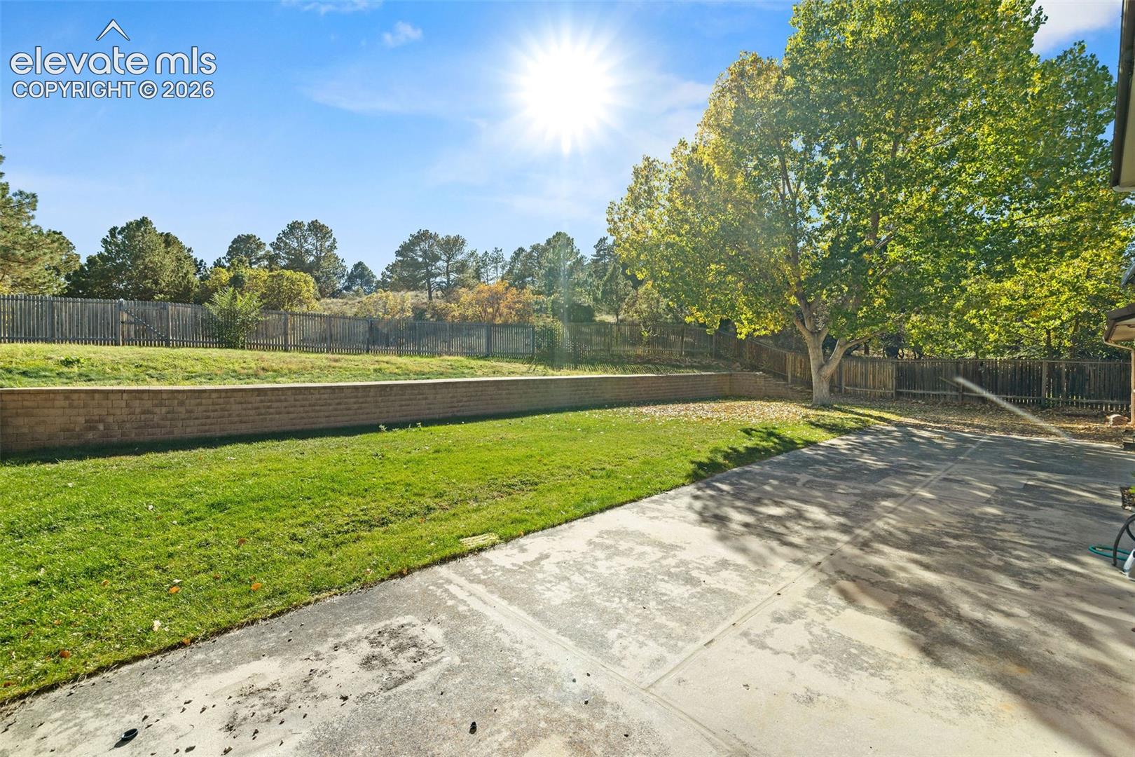 Spacious backyard featuring a concrete patio, terraced lawn, masonry retaining wall, and wood perimeter fencing