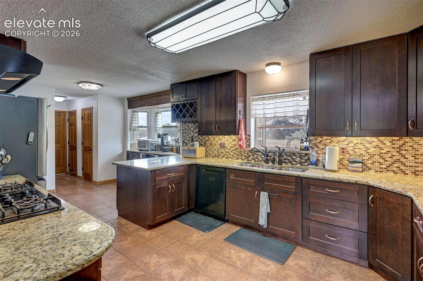 Kitchen featuring wood-finish cabinetry, granite countertops, tile flooring, and a mosaic tile backsplash