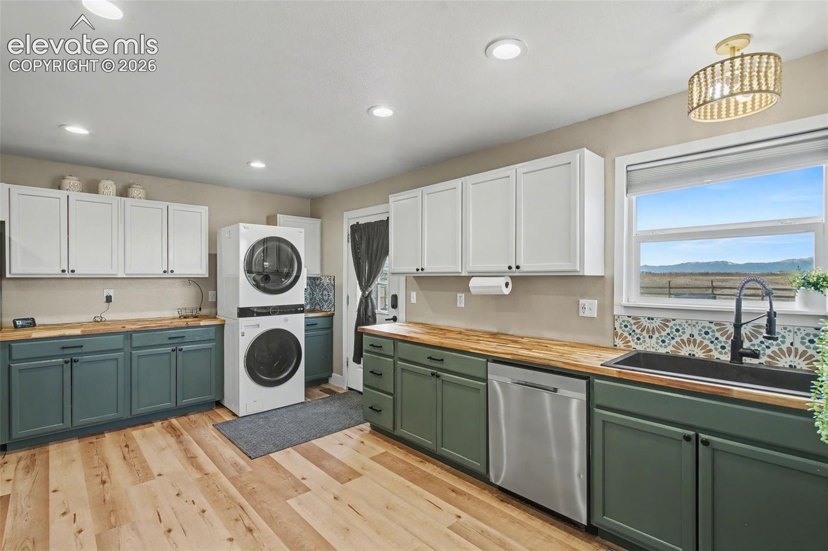 Dual-tone cabinetry, butcher block countertops, patterned tile backsplash, deep basin sink with gooseneck faucet, and wood-finish flooring
