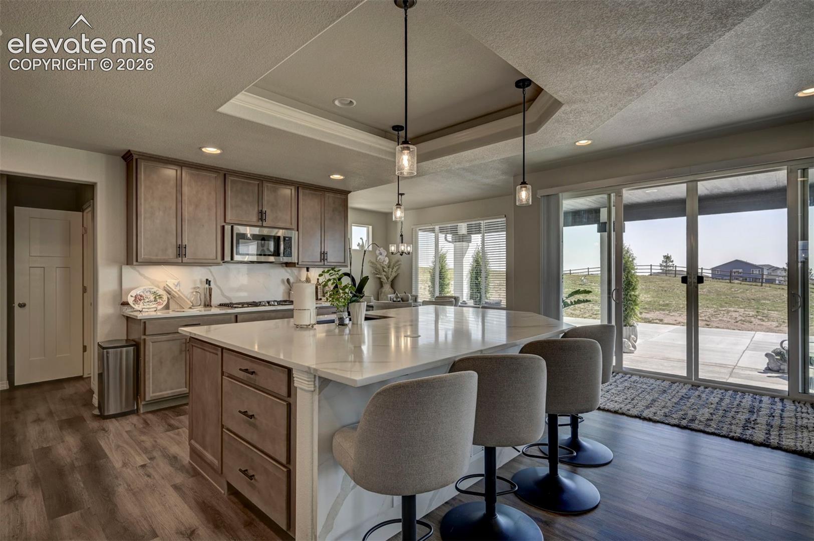 Kitchen featuring an expansive island with seating for three, stainless steel appliances, wood-finish flooring, recessed lighting, and sliding glass doors to the exterior
