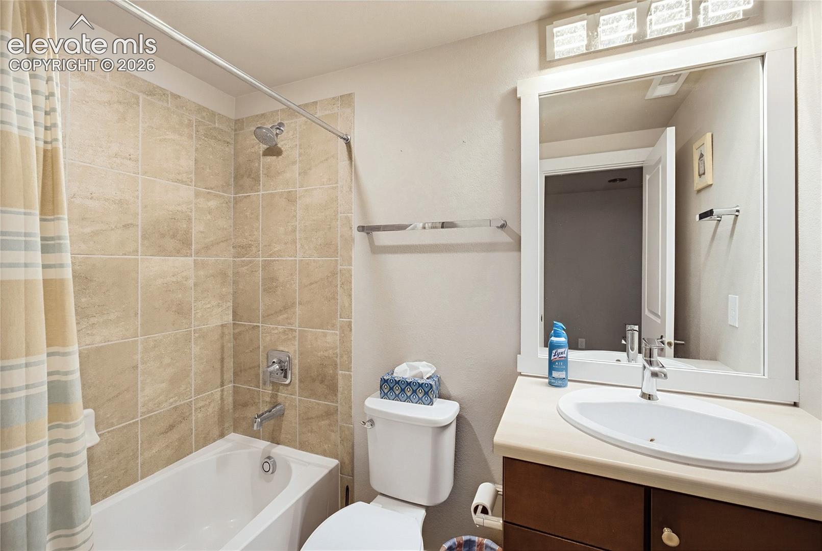 Bathroom featuring a white oval undermount sink, solid-surface countertop, dark wood-tone cabinetry, oversized framed mirror, and a tub-shower combination with square stone-finish wall tile