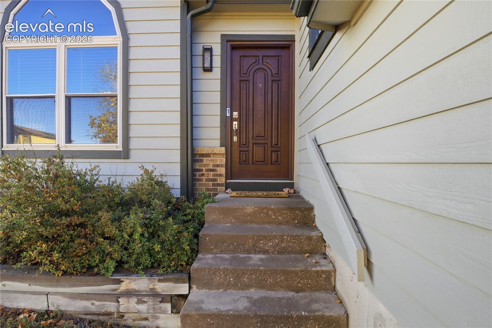 ENTRANCE FEATURING A MULTI-PANEL DARK WOOD DOOR, ARCHED-TOP WINDOW, LAP SIDING, CONCRETE STEPS WITH A METAL HANDRAIL, AND MASONRY DETAILING