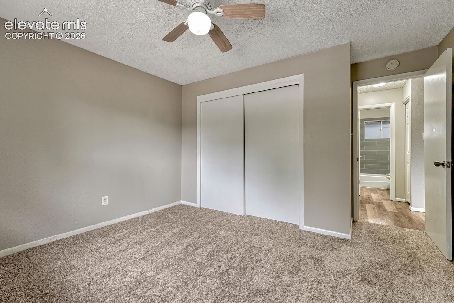 Carpeted flooring, ceiling fan with light fixture, sliding closet doors, and wood-finish flooring in the hallway
