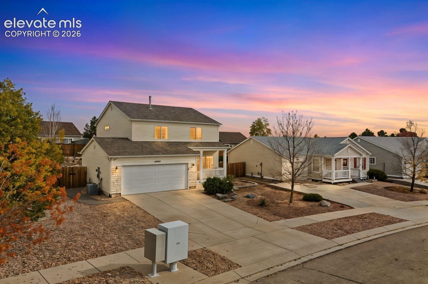 Two-story residence featuring light-toned horizontal siding, a multi-gabled asphalt shingle roof, a two-car attached garage, and a covered front porch with a wood-railing system
