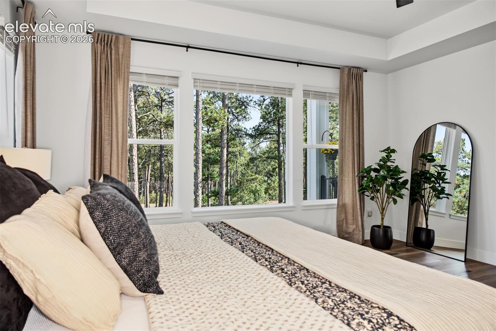 Spacious primary suite featuring an elegant tray ceiling, expansive windows framing beautiful tree views, and a peaceful, private retreat.
