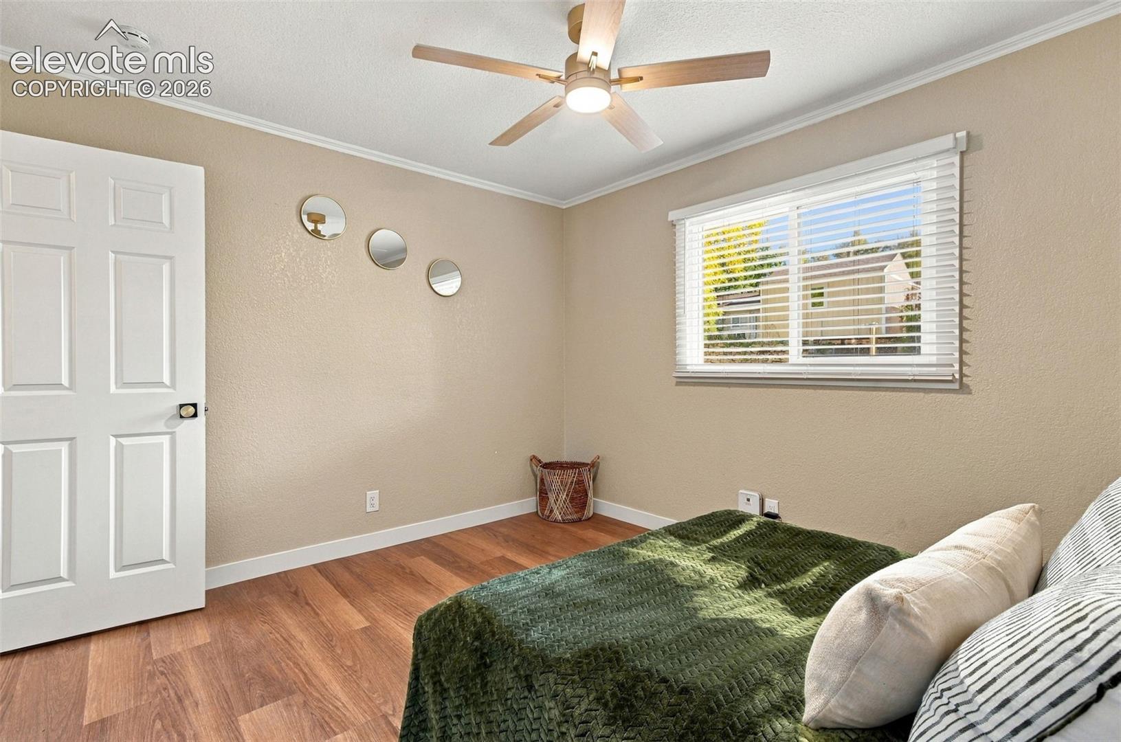 Wood-finish flooring, neutral wall tones, multi-paneled door, sliding window with horizontal blinds, and ceiling-mounted fan with integrated lighting