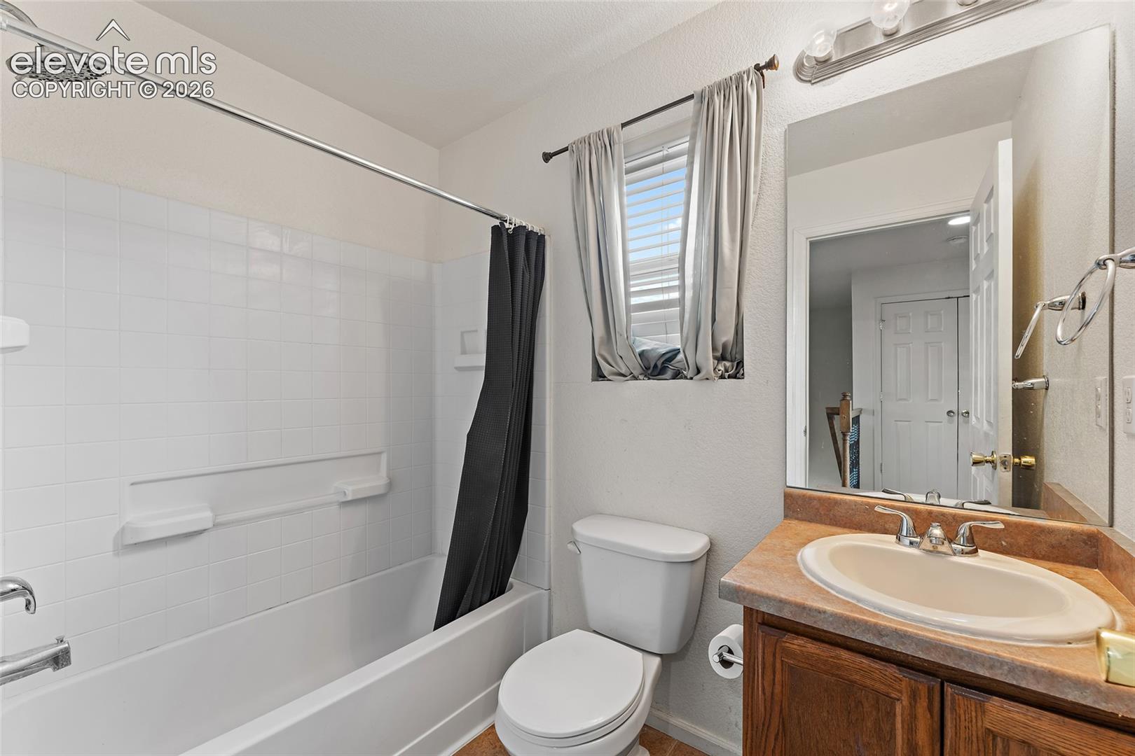 Bathroom featuring a white tile-surround tub, wood-finish vanity cabinet, oval integrated sink, large wall-mounted mirror, and multi-bulb vanity light fixture