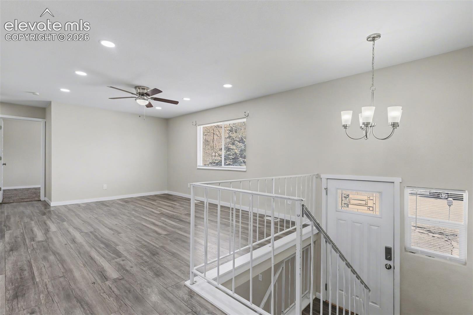 Interior space featuring wood-finish flooring, recessed lighting, a multi-arm chandelier, and a metal staircase railing