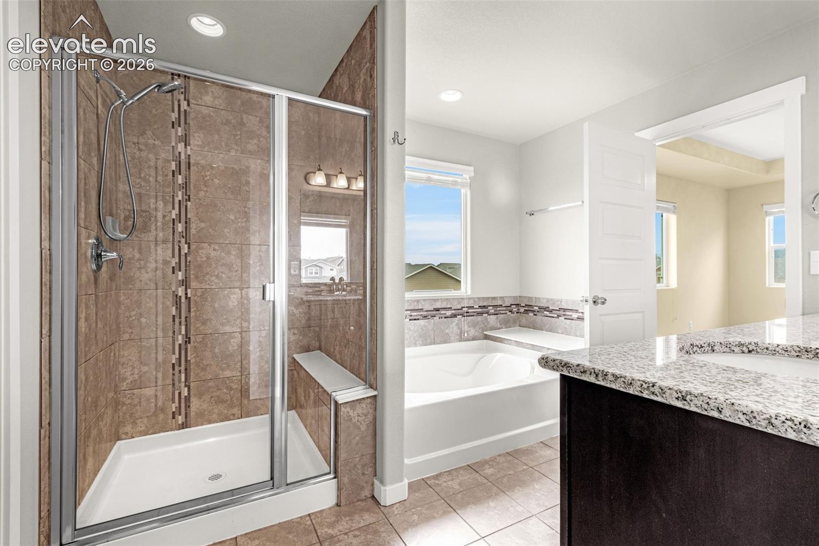 Enclosed shower with a built-in bench, a separate soaking tub, and a dual-sink vanity with granite countertops
