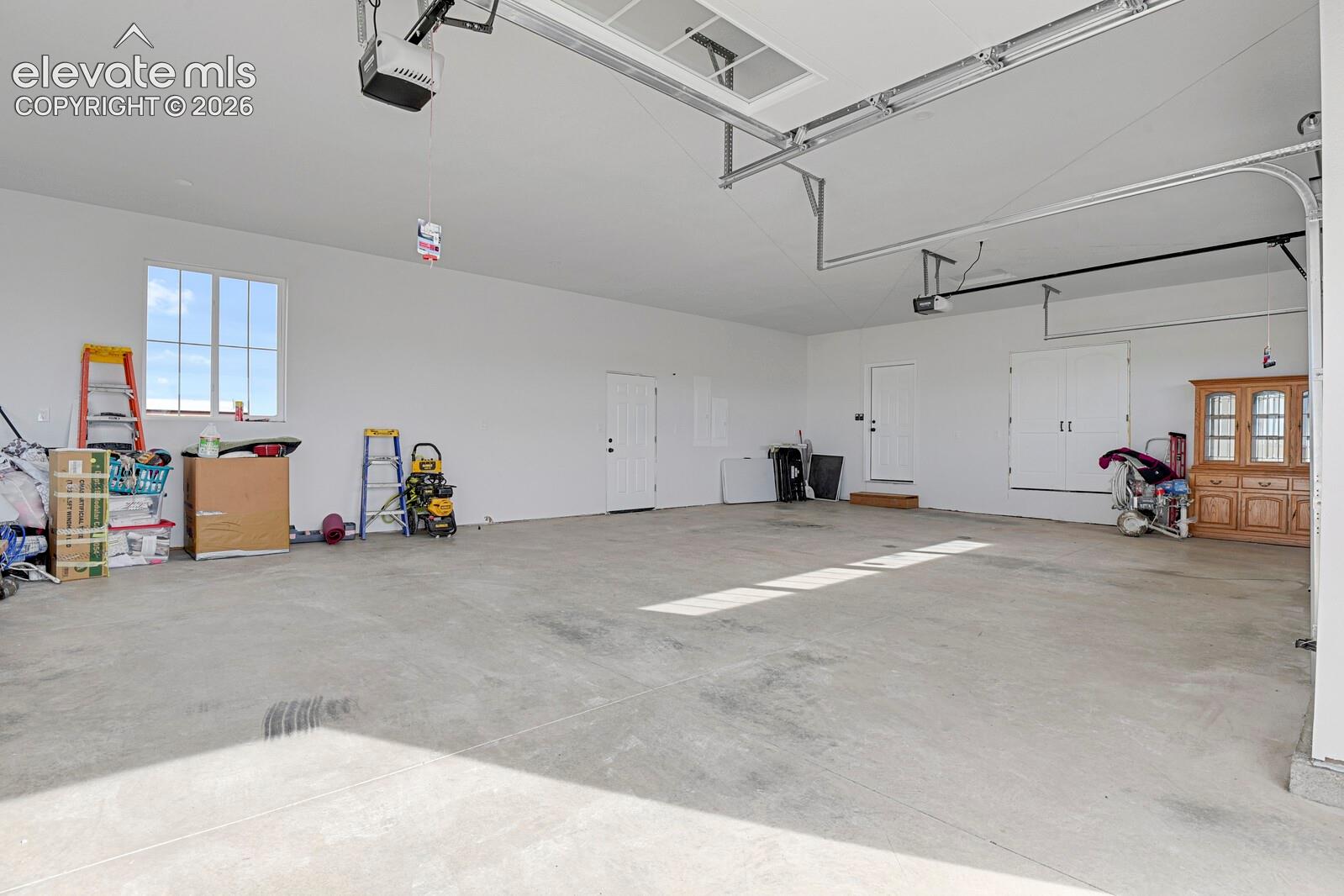 Multi-car garage featuring a concrete floor, high ceilings with motorized door openers, white walls, and a single-pane window