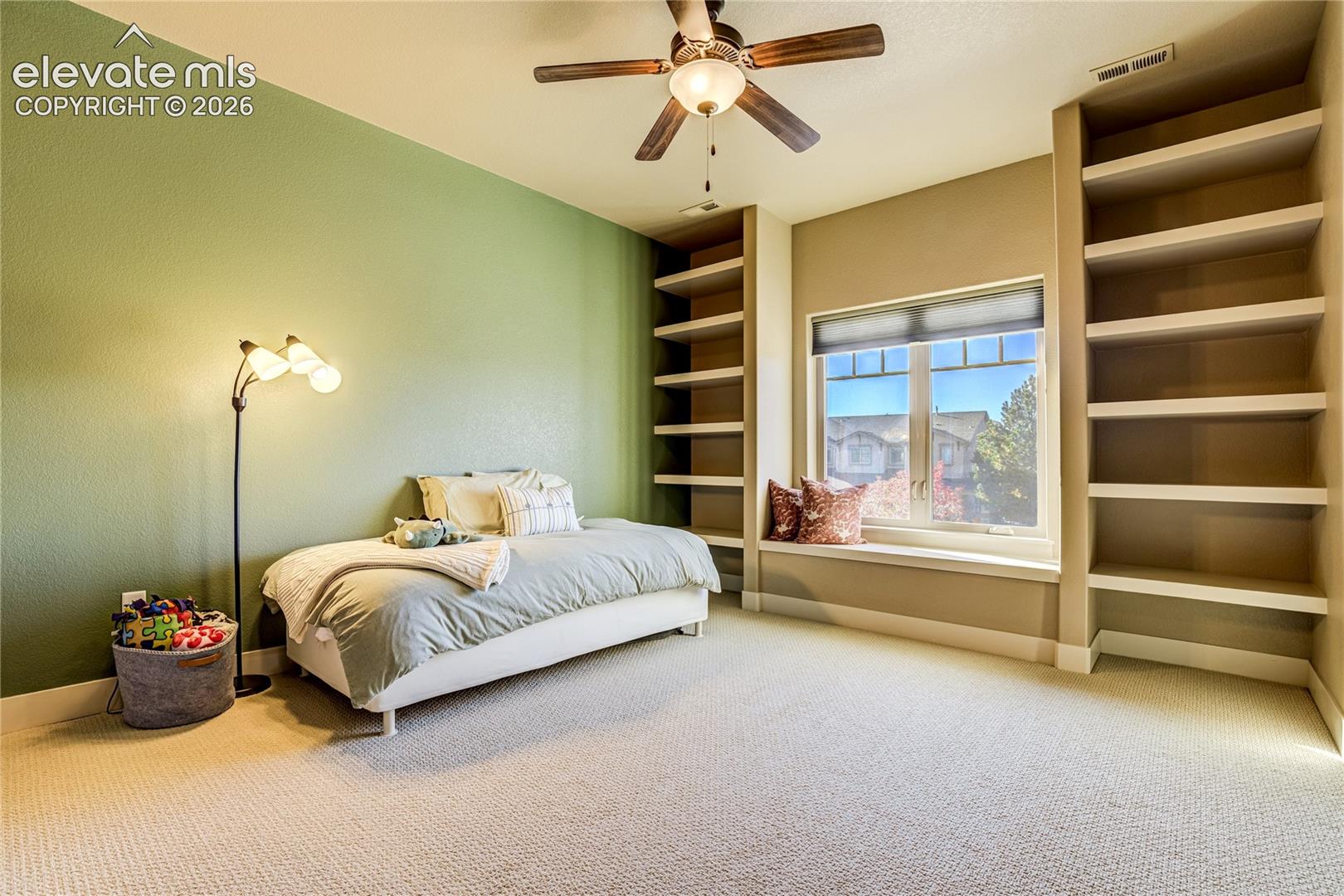 A charming window seat + custom built-in shelving distinguish this upper-level bedroom, creating a welcoming space for reading, relaxation or personal collections, with natural light enhancing its comfortable proportions.