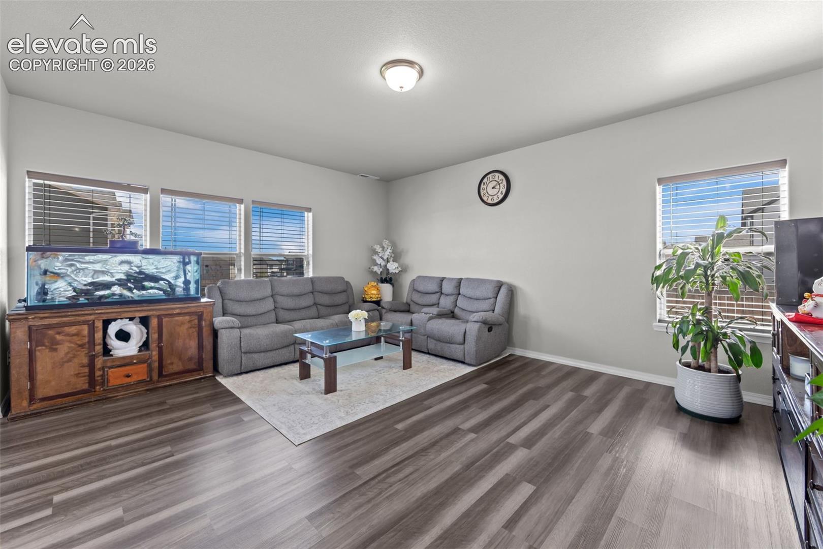 Spacious living area featuring wood-finish flooring, ample natural light from multiple windows, and a semi-flush mount ceiling light