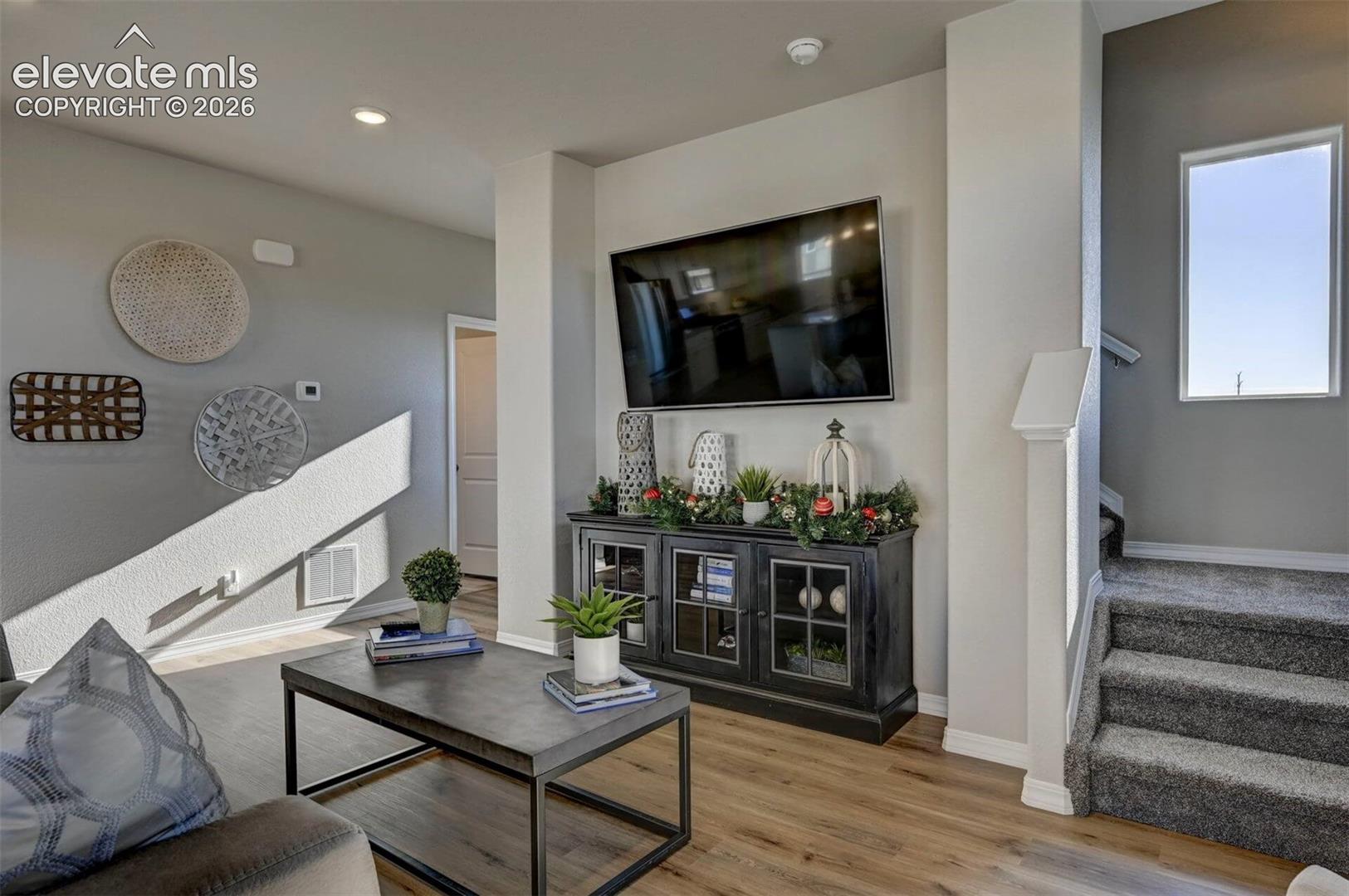 Living area featuring wood-finish flooring, vaulted ceiling, recessed lighting, and carpeted staircase with a windowed landing