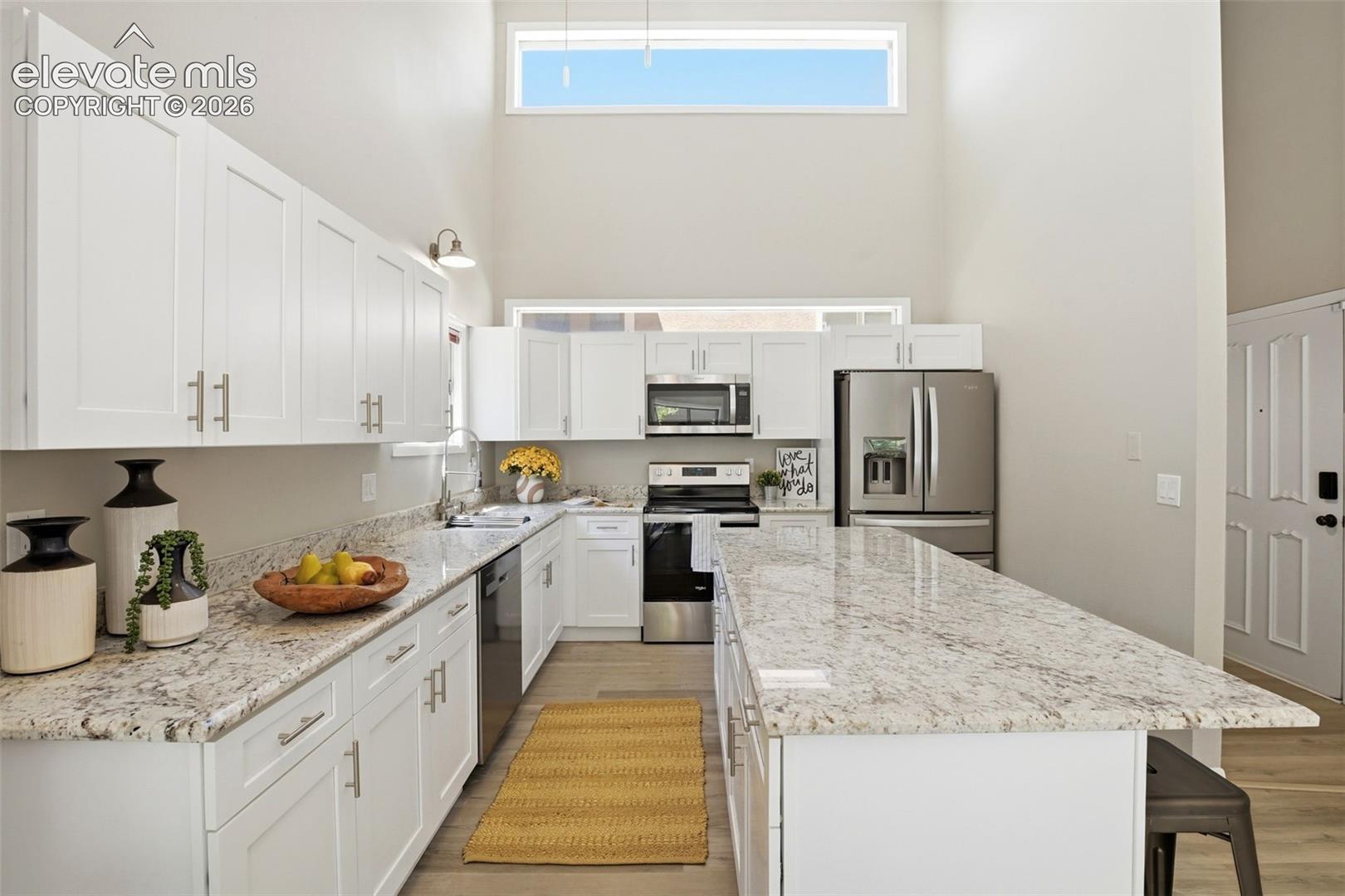 Modern kitchen featuring white cabinetry, light-colored granite countertops, and stainless steel appliances