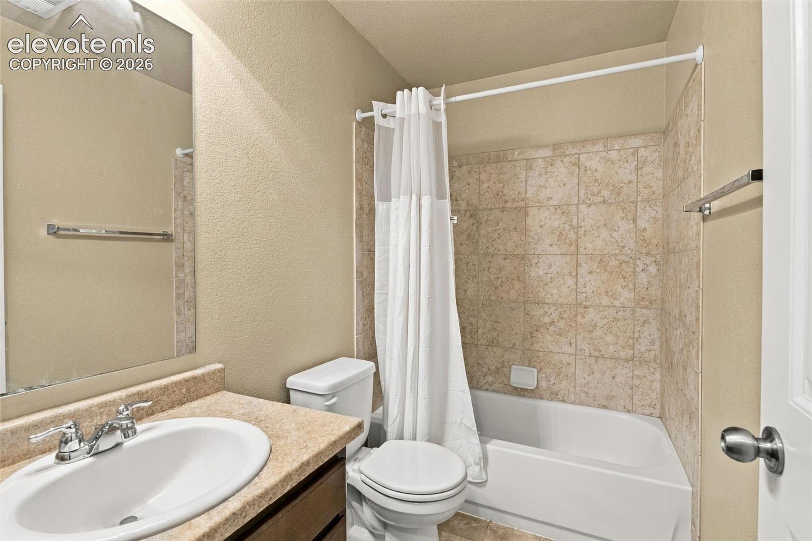 Bathroom featuring a solid-surface vanity countertop, drop-in sink with dual-handle chrome faucet, wall-mounted mirror, and a tub-shower combination with ceramic tile surround