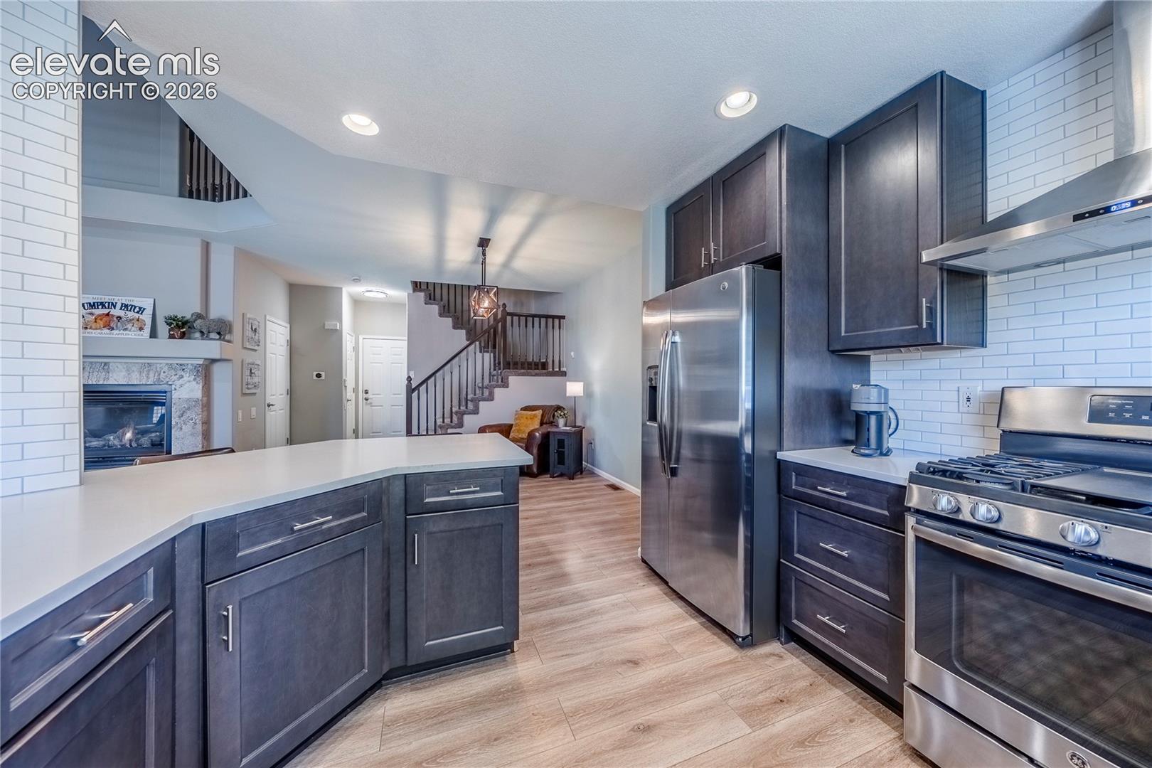 Kitchen featuring dark wood cabinetry, solid surface countertops, a white tile backsplash, stainless steel appliances, and wood-finish flooring
