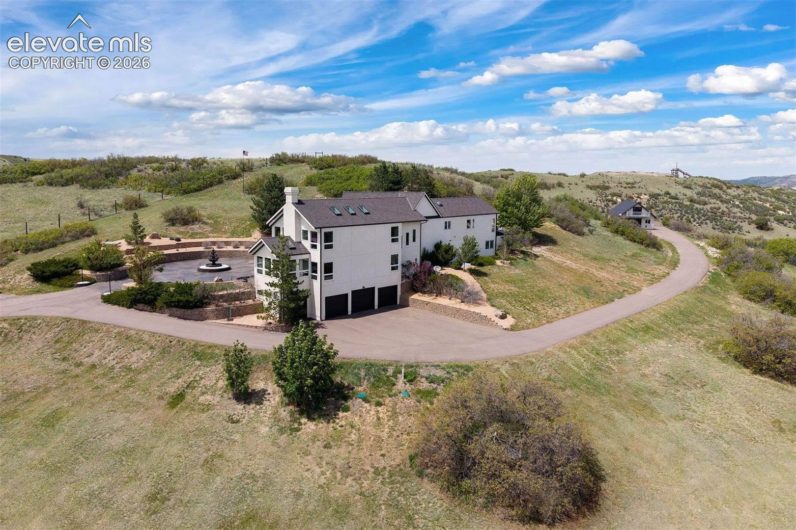 Aerial view of the rear of the estate showing the 4-car garage, circular motor court, patio, and sweeping asphalt driveway winding through the acreage.