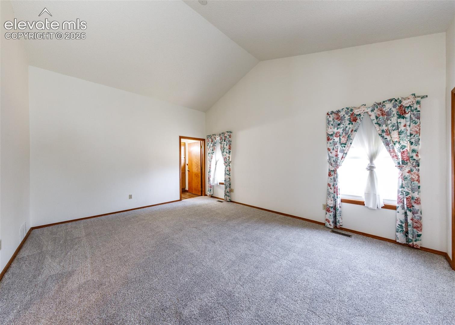 Vaulted ceiling with white paint, light gray carpet, and wood trim