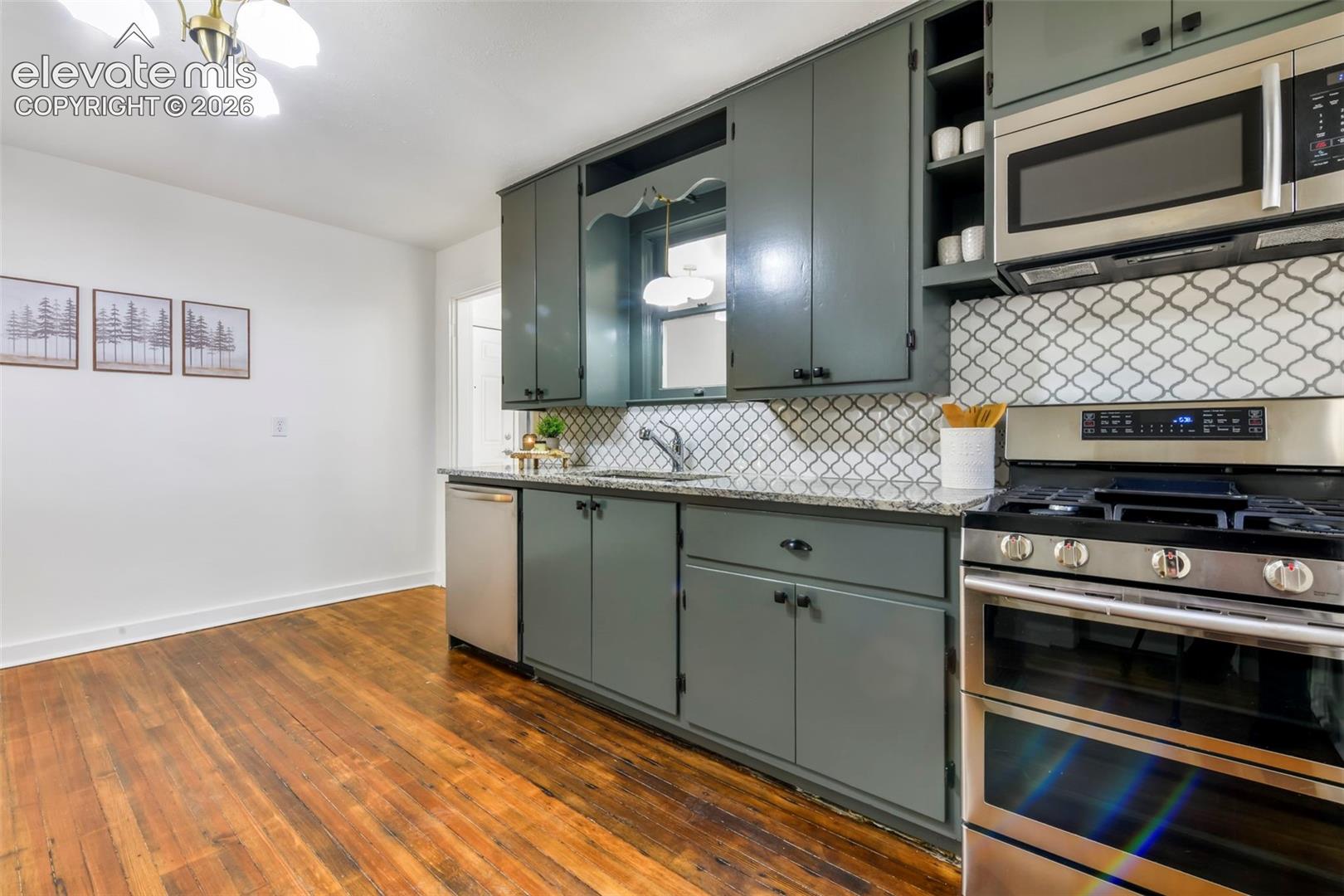 Kitchen featuring painted cabinetry, stone-finish countertops, geometric-pattern tile backsplash, stainless steel appliances, and wood-finish flooring