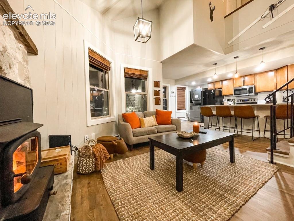 Open-concept living space featuring wood-finish flooring, a stone fireplace with a wood-burning stove, and vaulted ceilings