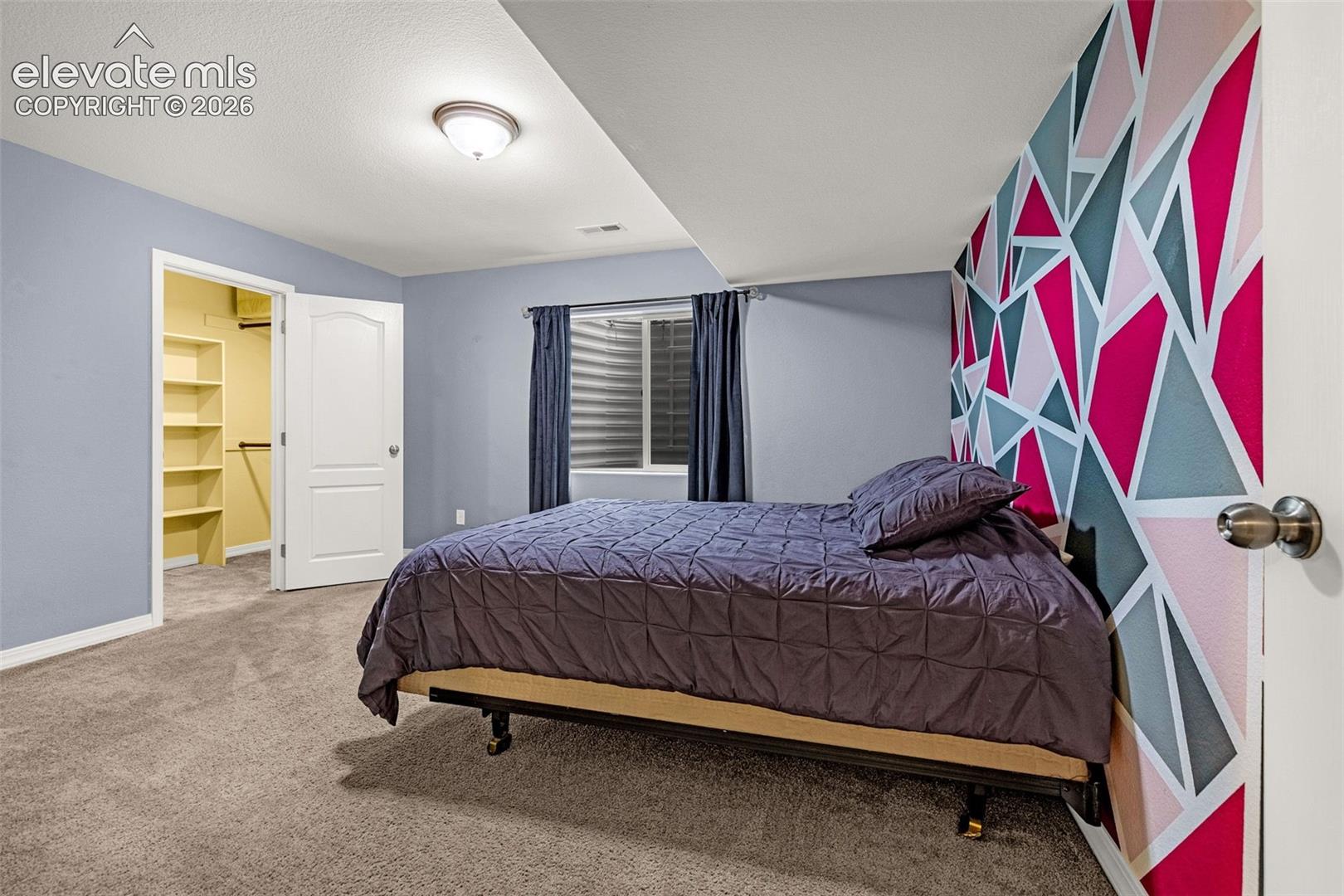 Neutral wall tones, geometric accent wall, wall-to-wall carpeting, window with a below-grade window well, and walk-in closet with built-in shelving