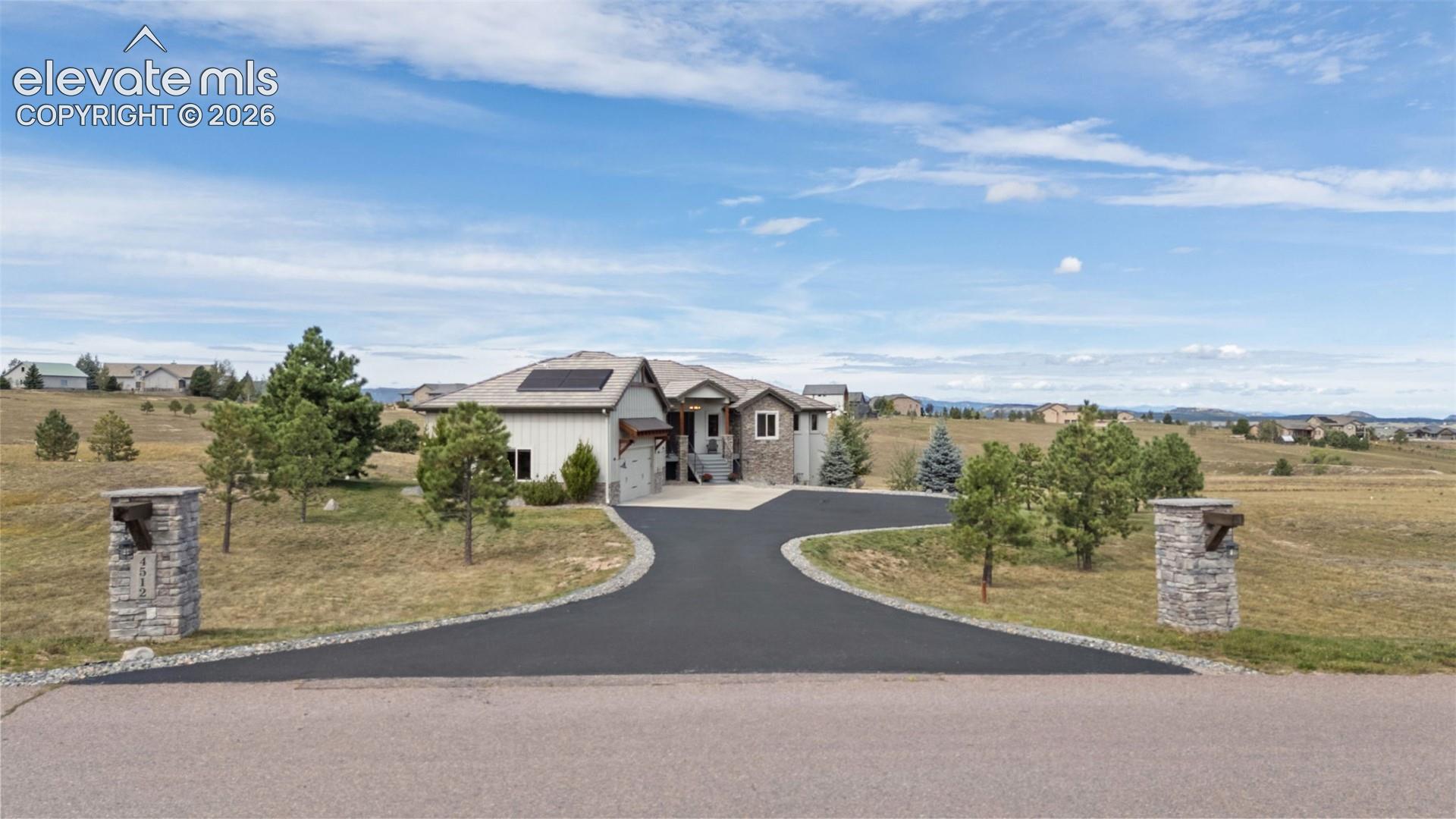Spacious property featuring a paved circular driveway, stone-clad entry pillars, solar panels on the roof, and a multi-level architectural design