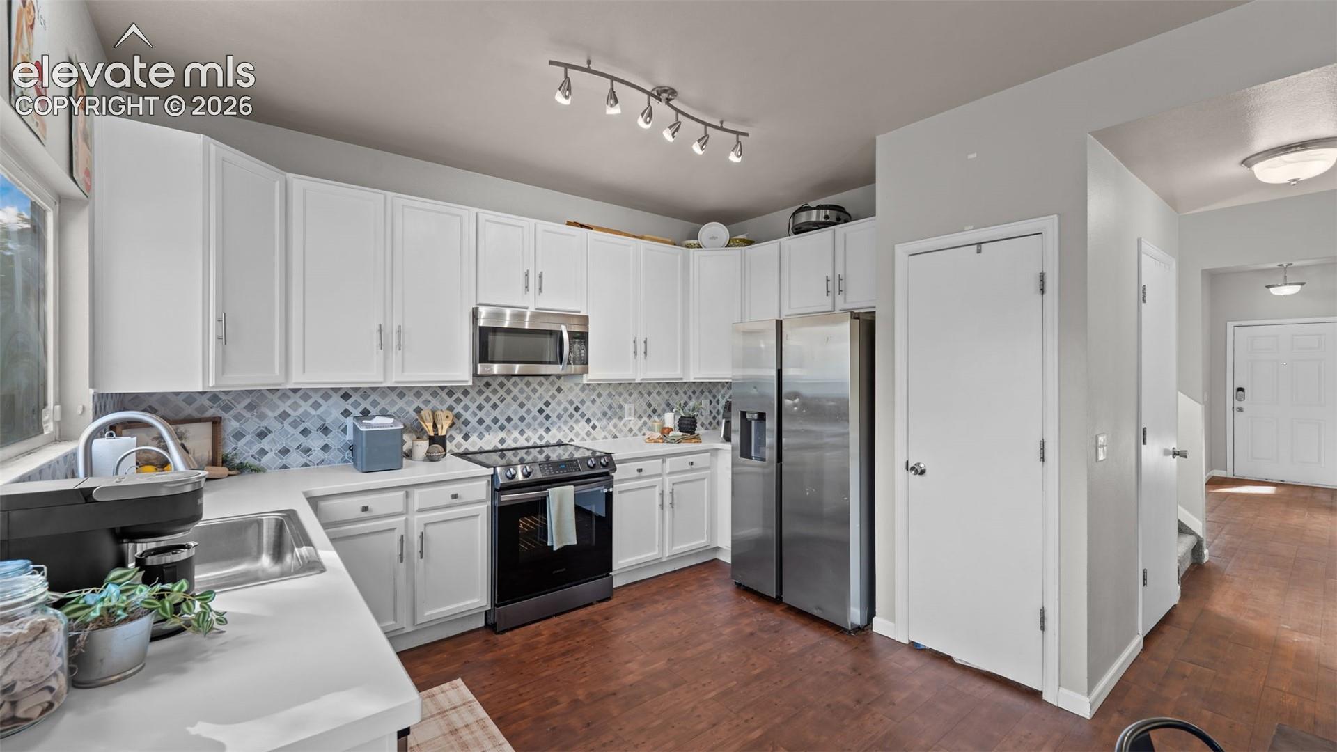 Contemporary kitchen featuring white cabinetry, light-toned countertops, stainless steel appliances, a patterned backsplash, and wood-finish flooring