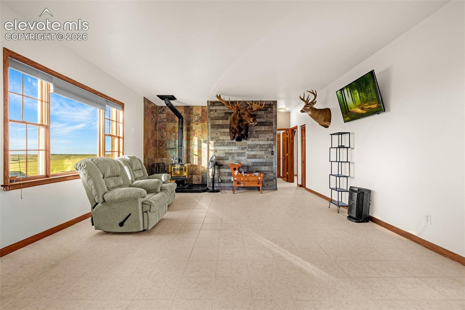 Spacious interior with neutral-toned flooring, large window offering expansive outdoor scenery, and a built-in wood-burning stove with a stone surround