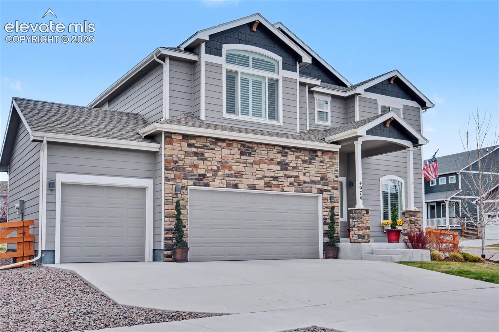 Multi-level residence featuring gray siding, stone facade accents, a front entry porch with stone columns, and a two-car garage