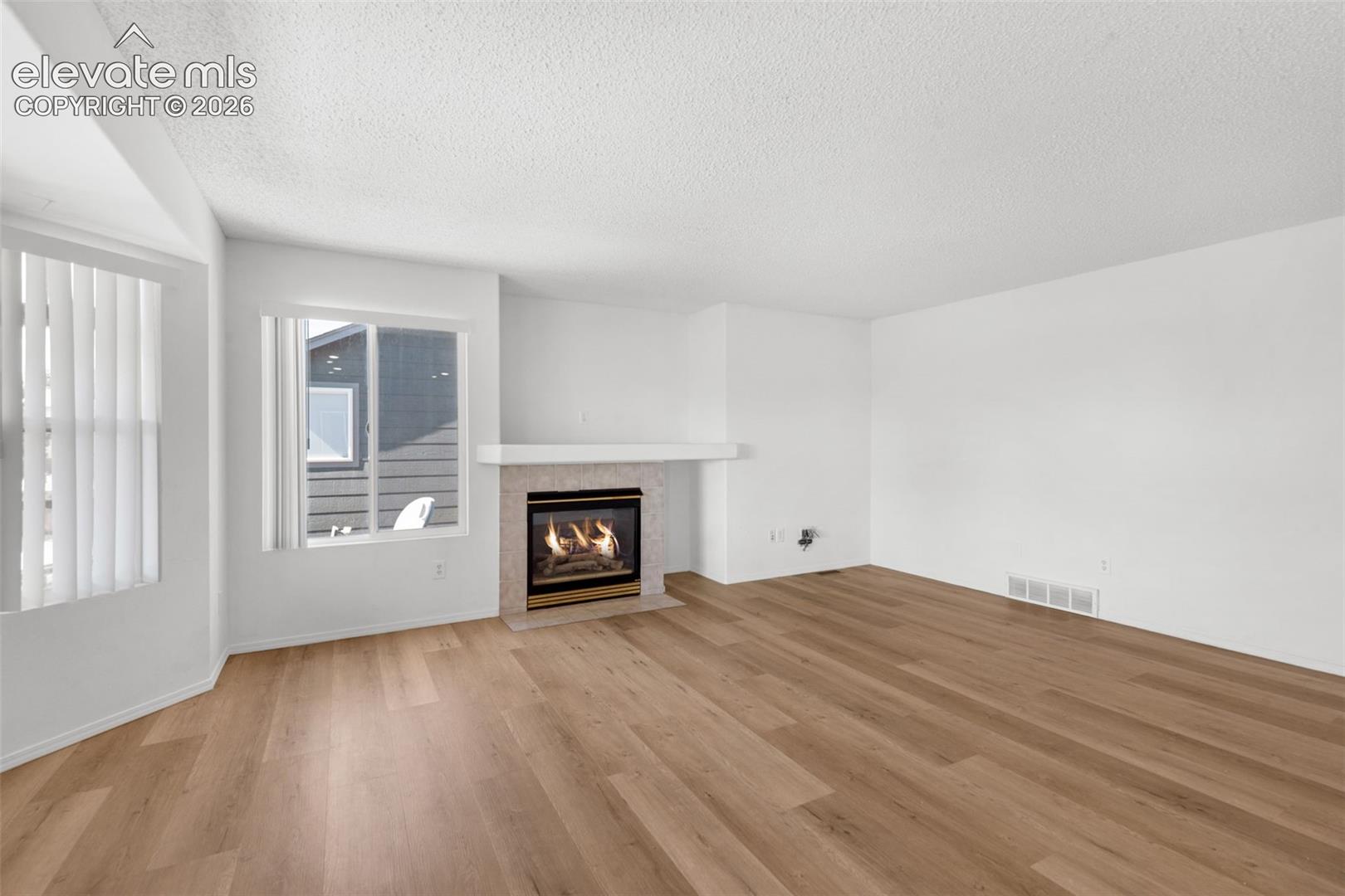Wood-finish flooring, white walls, and a fireplace with a light-toned tile surround